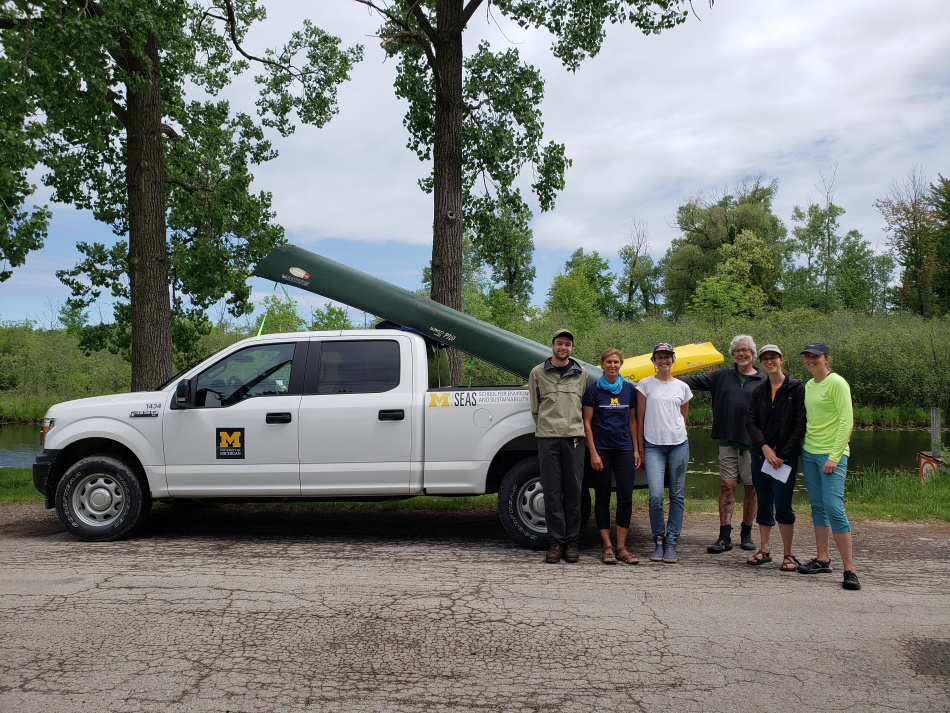Team members and clients standing in front of the SEAS Facilities truck with kayaks and a canoe loaded in the bed