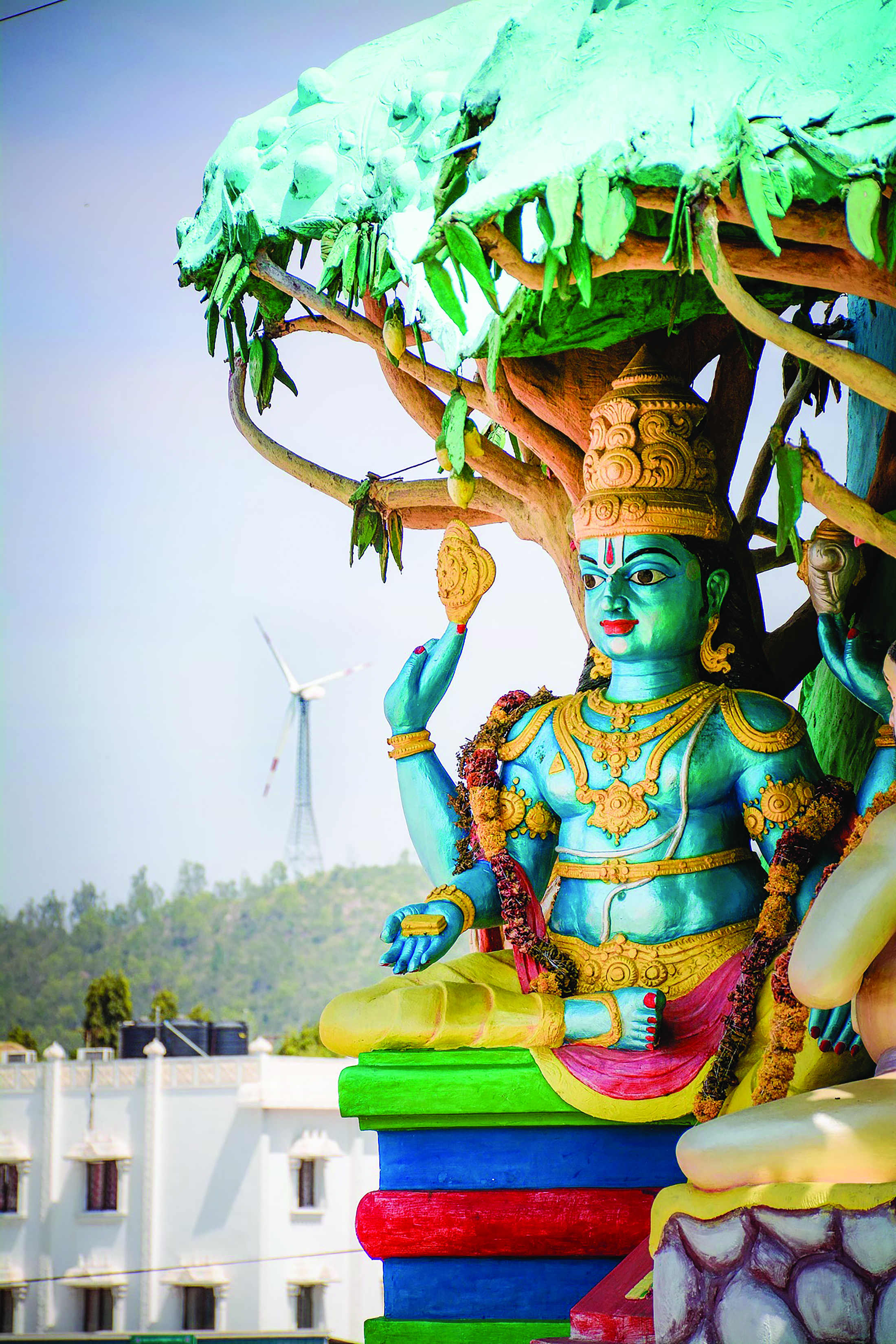 Wind turbines in the hills of the holy city of Tirumala, India, with a wooden figure of Vishnu, one of the principal deities of Hinduism, in the foreground.