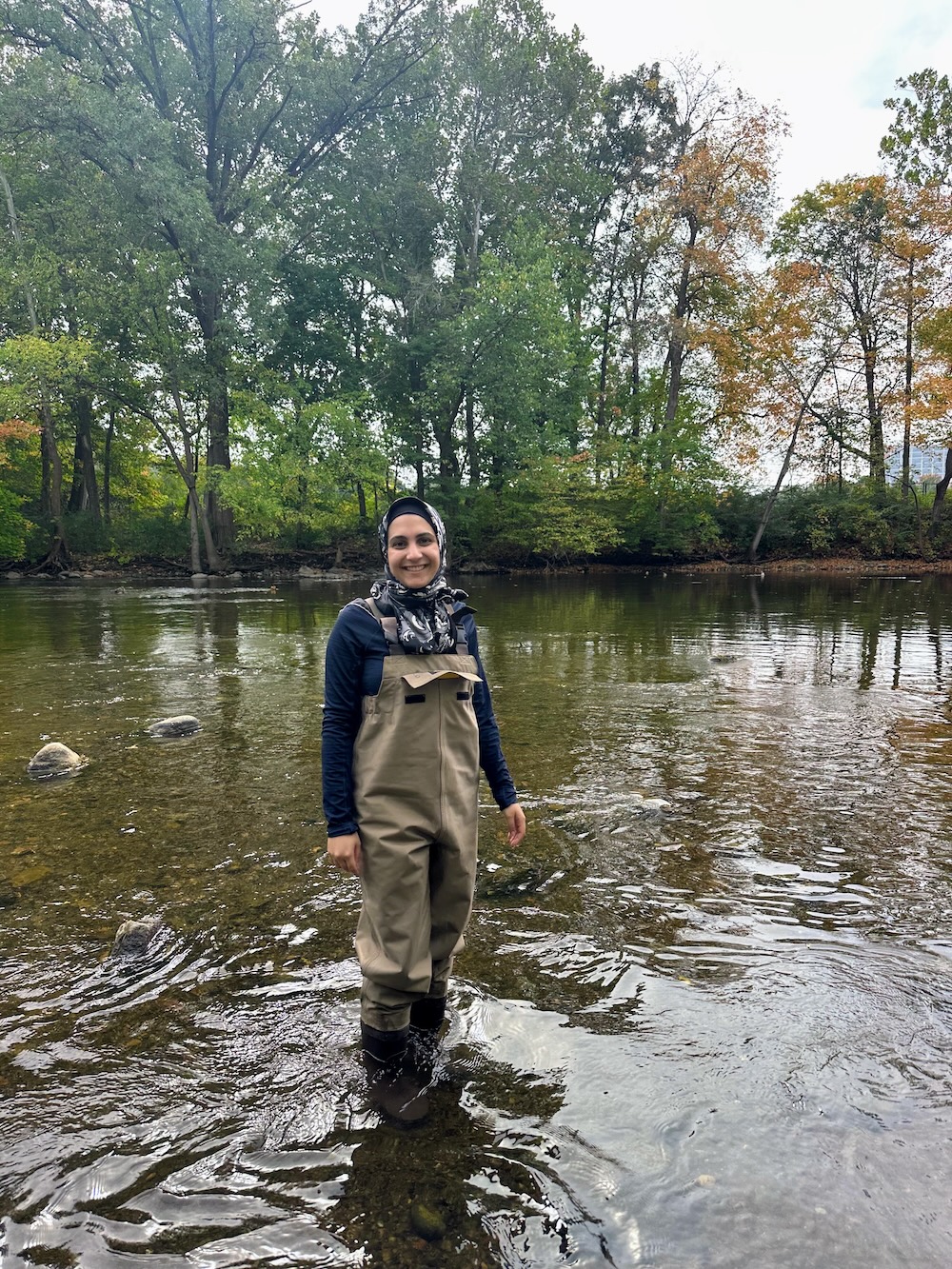 Melika Sizar (MS ’26) in a river, with a forest in the background.